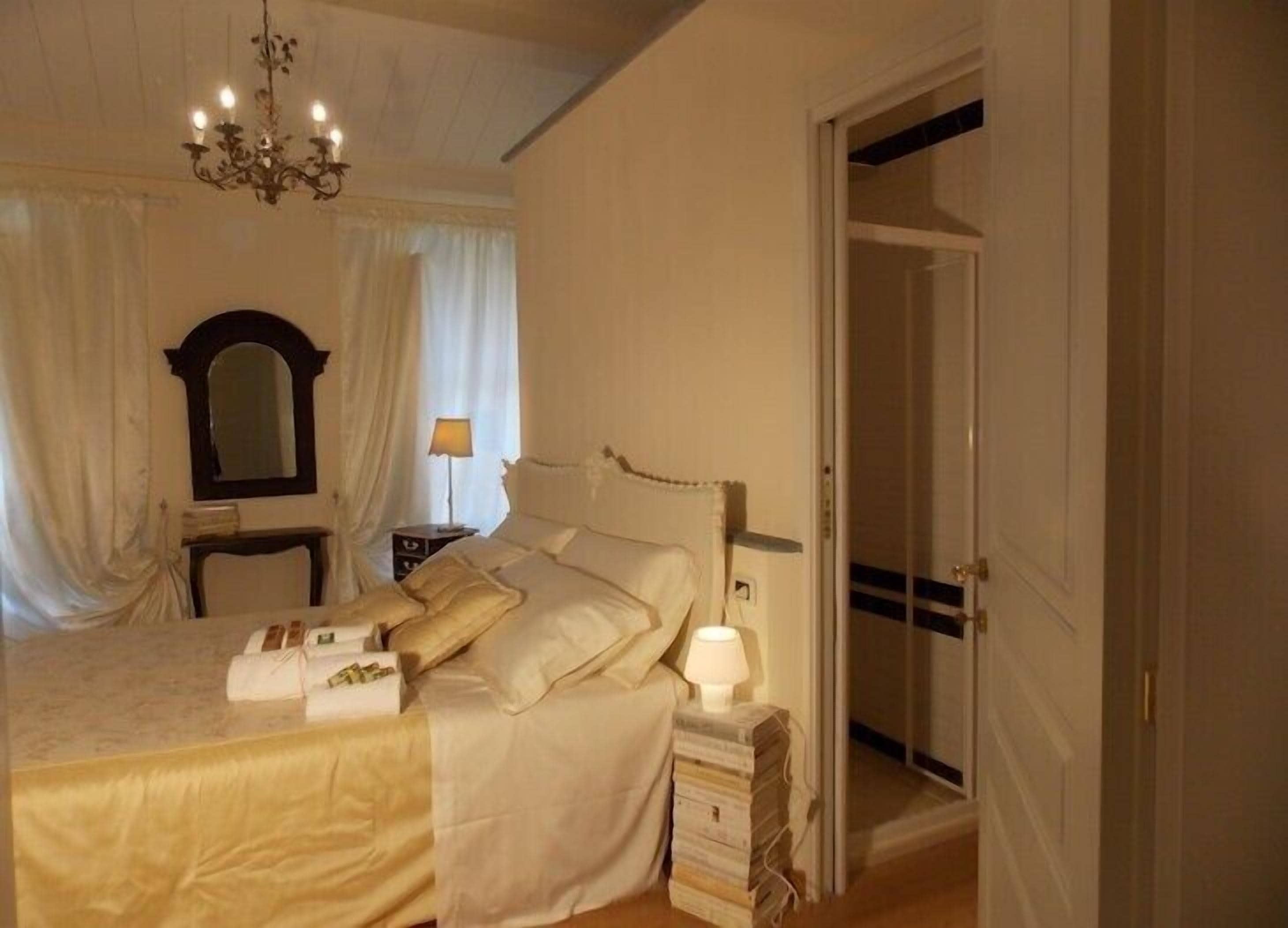 A bedroom with a large bed, a bedside table with a lamp, a mirror, and a door leading to another room.