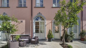 A building with a pink facade, a central arched doorway, and a patio area with outdoor furniture and potted plants. - B&B Di Camilla (Pisa)