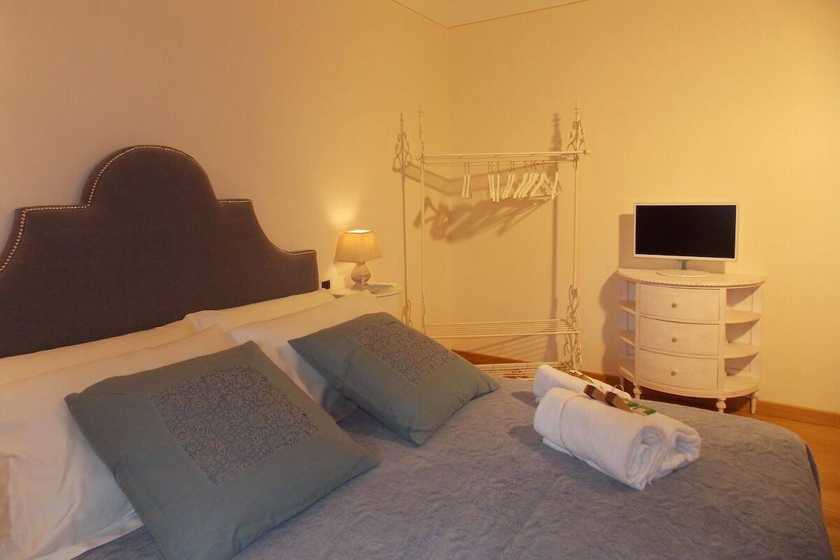Un lit bien fait, avec des oreillers, une lampe de chevet, une télévision et une commode blanche dans une chambre d’hôtel.