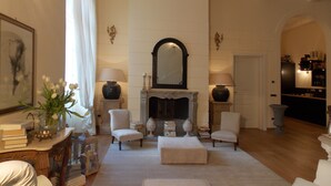 A spacious living room with a fireplace, two armchairs, a sofa, and a coffee table. There is a bookshelf and a dining area visible in the background. - B&B Di Camilla (Pisa)
