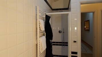 A bathroom with white tiled walls, a black and white shower area, and a visible towel rack with towels.