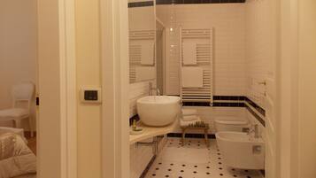 A bathroom with a large sink, a bathtub, and a toilet. There is a mirror above the sink and a towel rack above the bathtub. The floor has a black and white tile pattern.