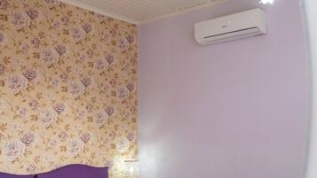 A bedroom with two beds, a floral wallpaper, a purple bedspread, a white air conditioning unit, and a chandelier.
