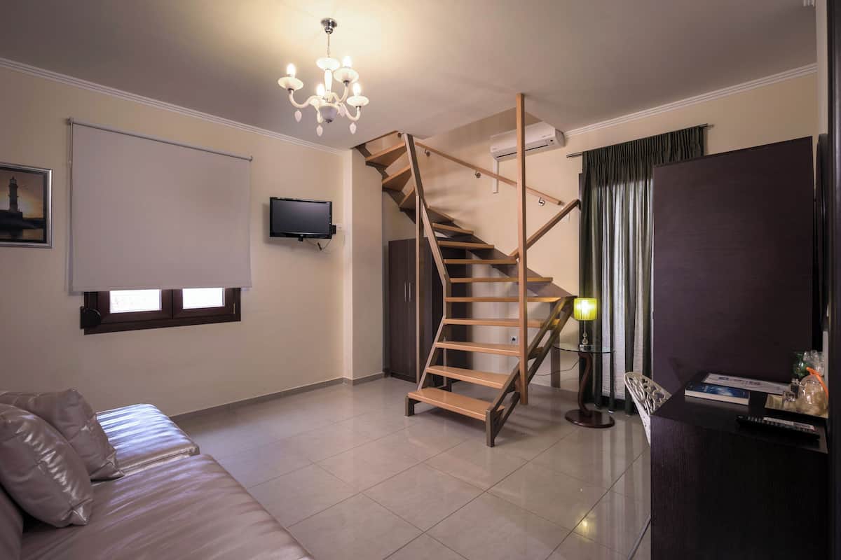 A modern living room with a wooden staircase, a flat-screen TV, a sofa, and a desk with a lamp.