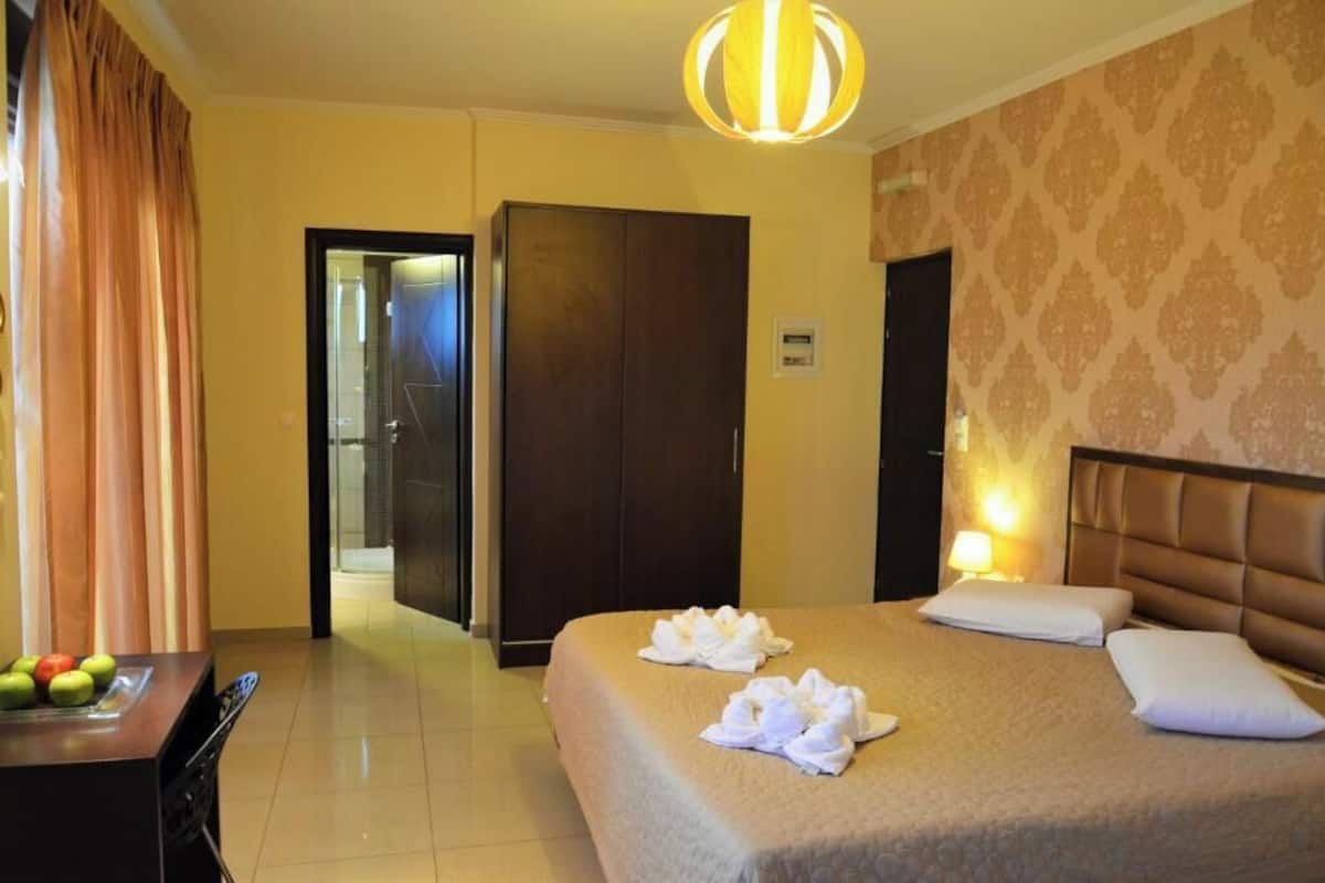 A hotel room with a bed, a desk with fruit, a wardrobe, and a bathroom visible through an open door.