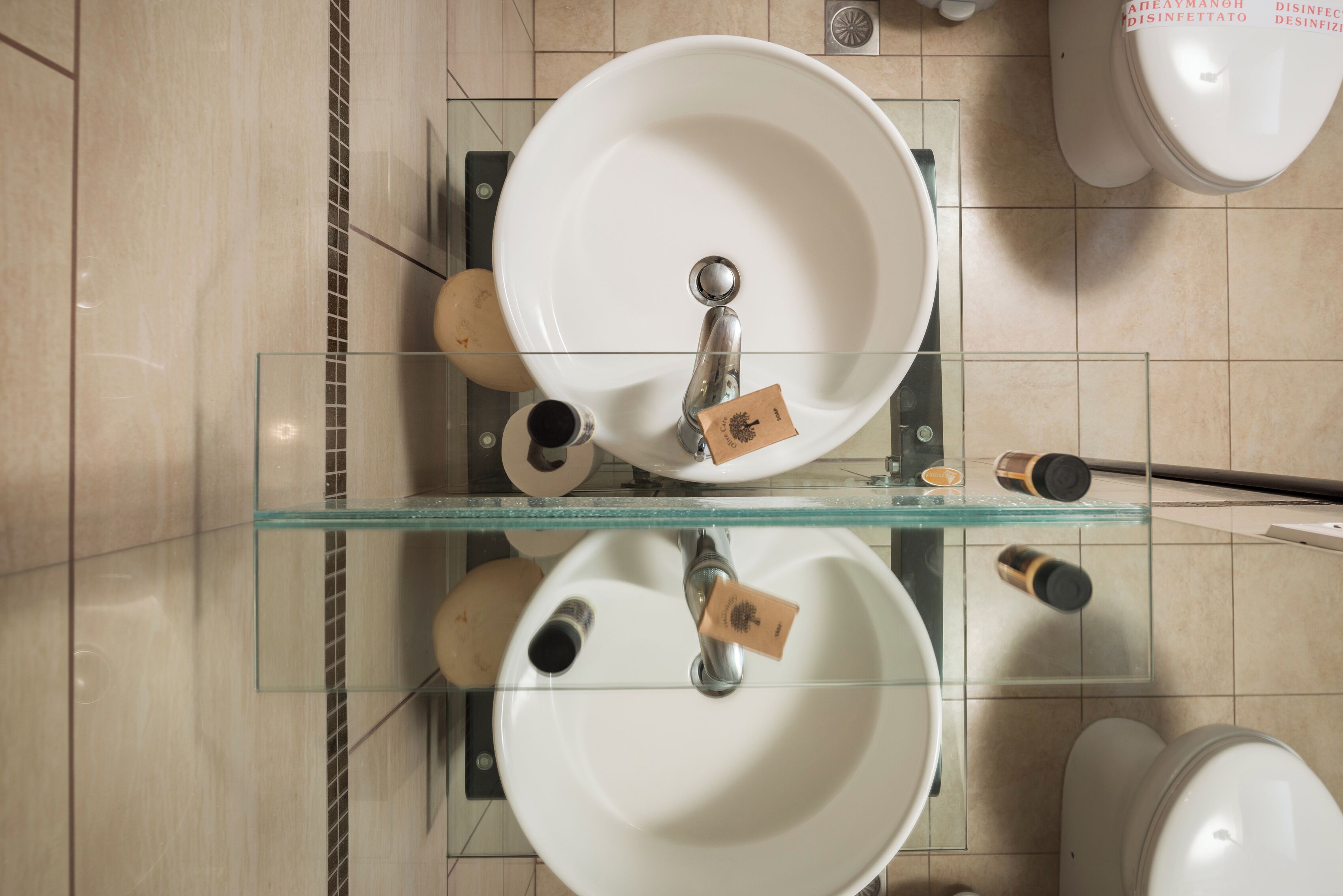 Un baño con dos lavamanos, una repisa de vidrio y un inodoro.