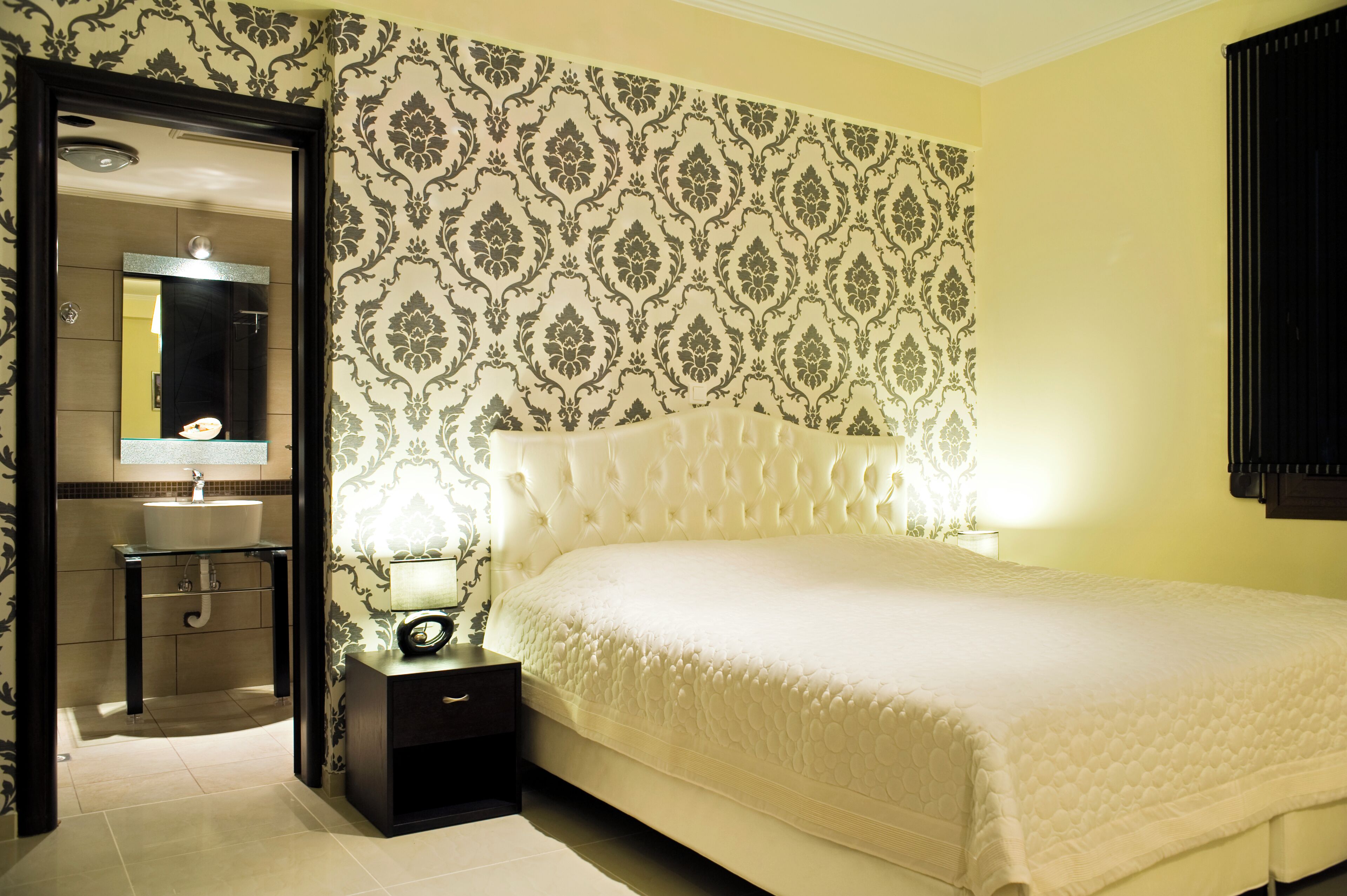 A bedroom with a large bed, a bedside table, a nightstand, a mirror, and a bathroom with a sink and toilet.