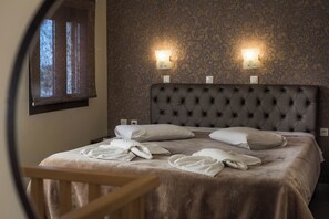 A neatly made bed with white linens and towels, a tufted headboard, and two wall-mounted light fixtures. - Areti Suites Chania (Chania)