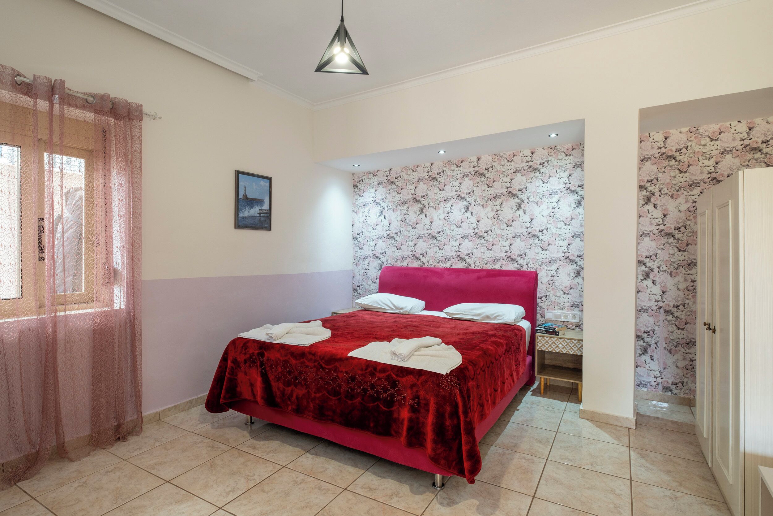 Un dormitorio con colcha roja, cabecera rosa y pared cubierta de papel tapiz floral.