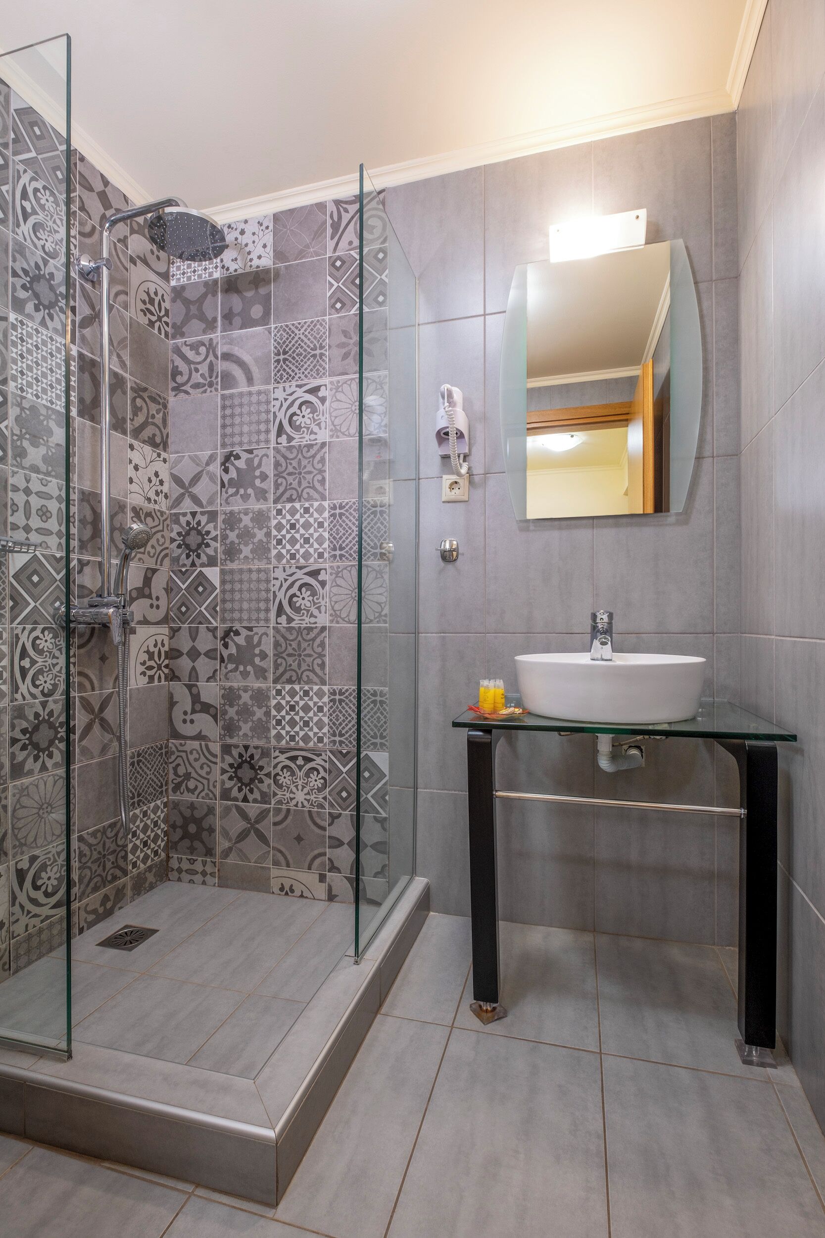 A bathroom with a glass shower enclosure, patterned tiles, a white sink, and a mirror above it.