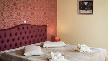 Una cama bien hecha con cabecera roja, almohadas blancas y toallas sobre un edredón color beige.