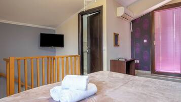 Un dormitorio con cama, baranda de madera, televisor montado en la pared y ventana con persianas.