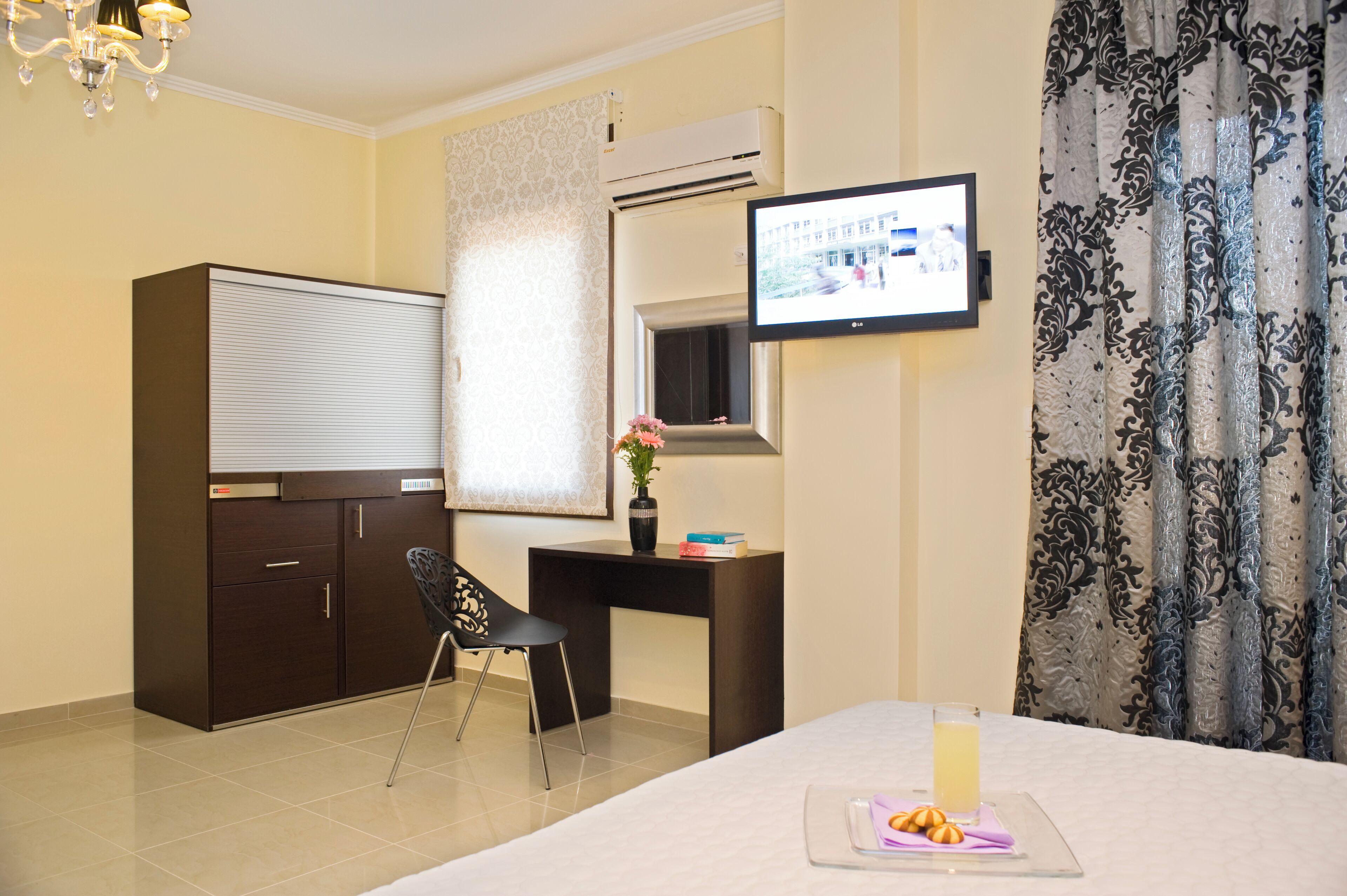 Habitación de hotel con cama, escritorio, silla, aire acondicionado, televisor y ventana con cortinas.