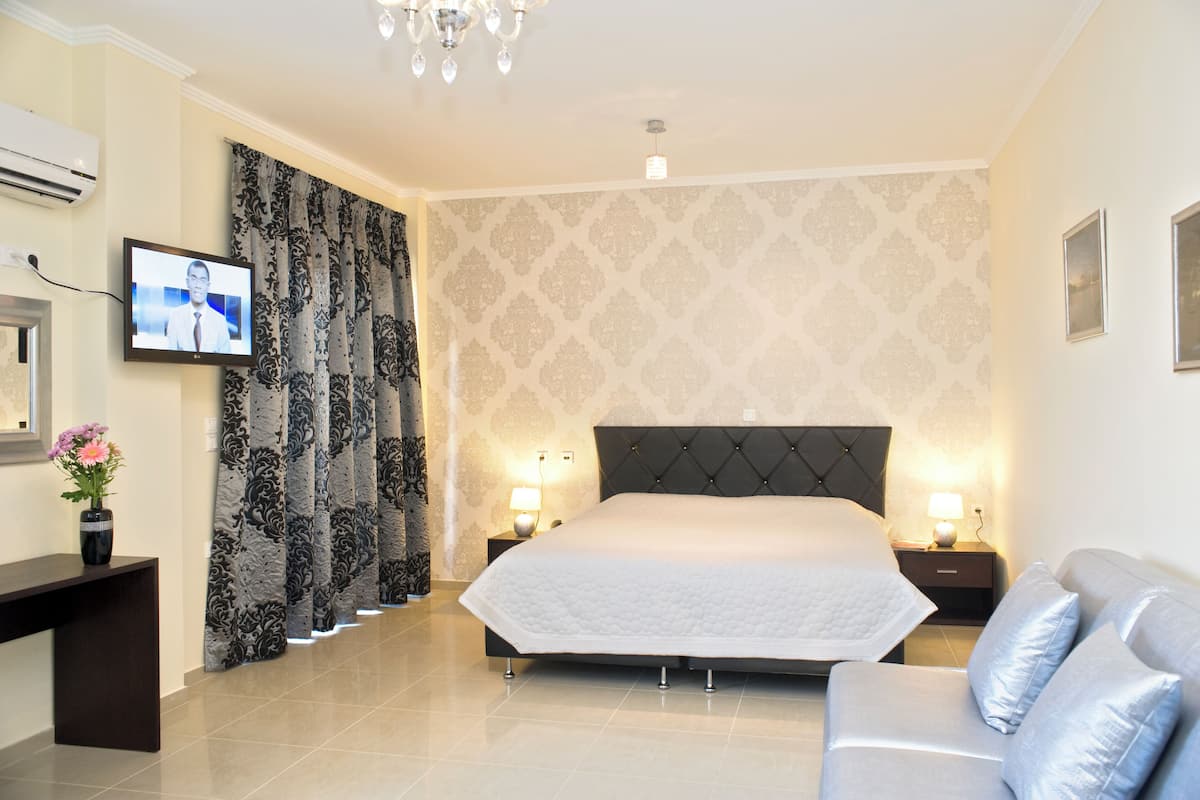 A modern hotel room with a large bed, a sofa, a TV, and a desk with a vase of flowers.