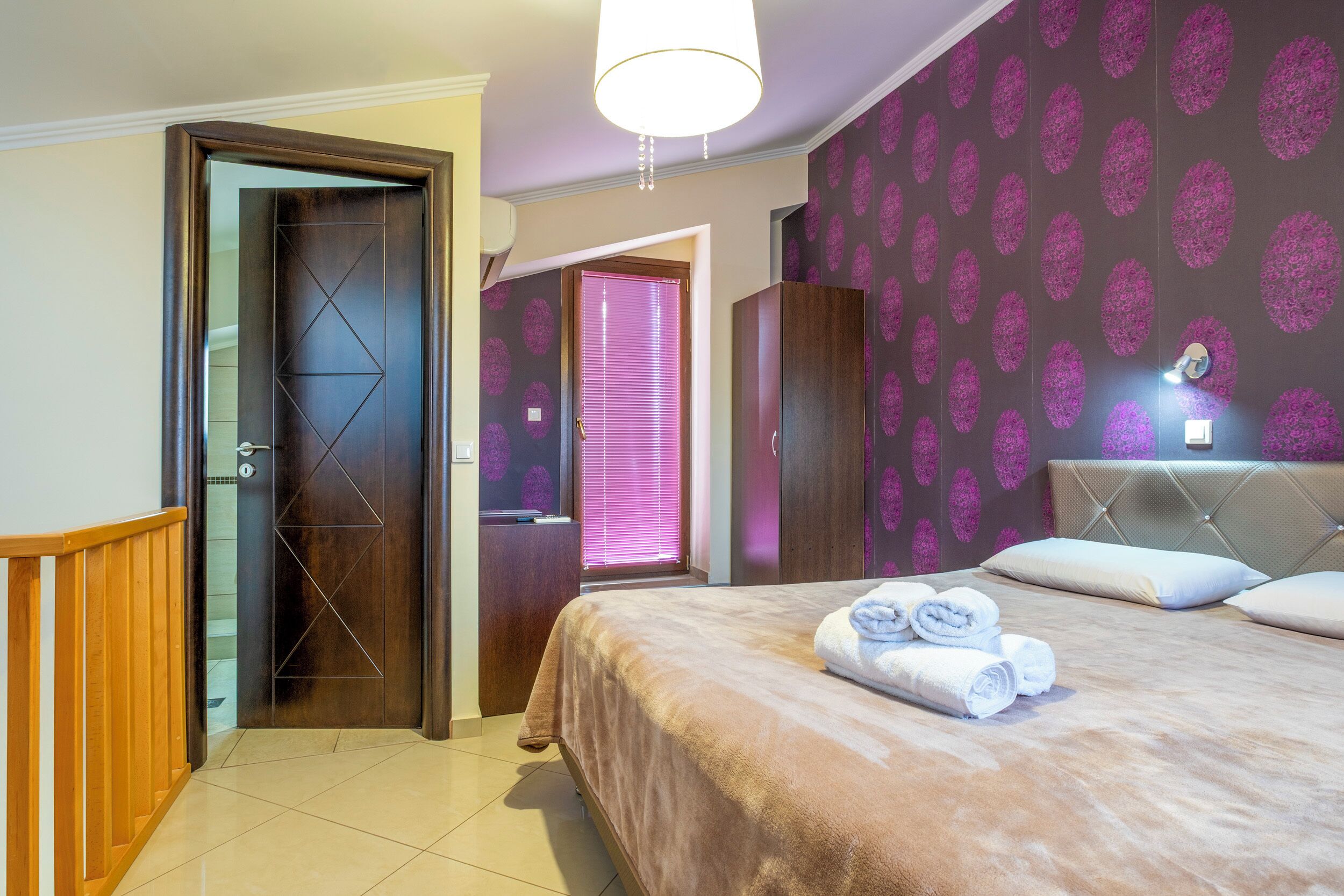 Una habitación de hotel con cama, una puerta de madera, un baño y una pared con estampado floral.