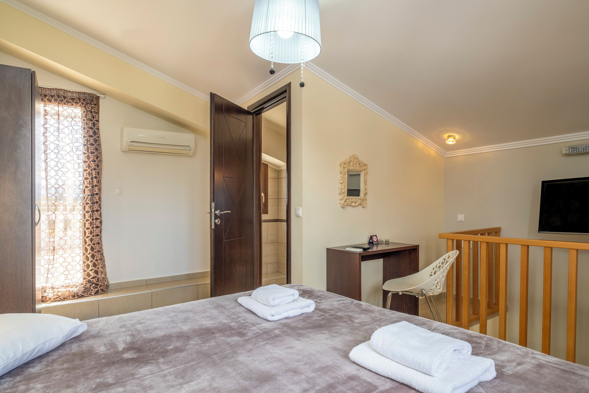 A hotel room with a bed, a desk, a chair, a TV, and an air conditioning unit.