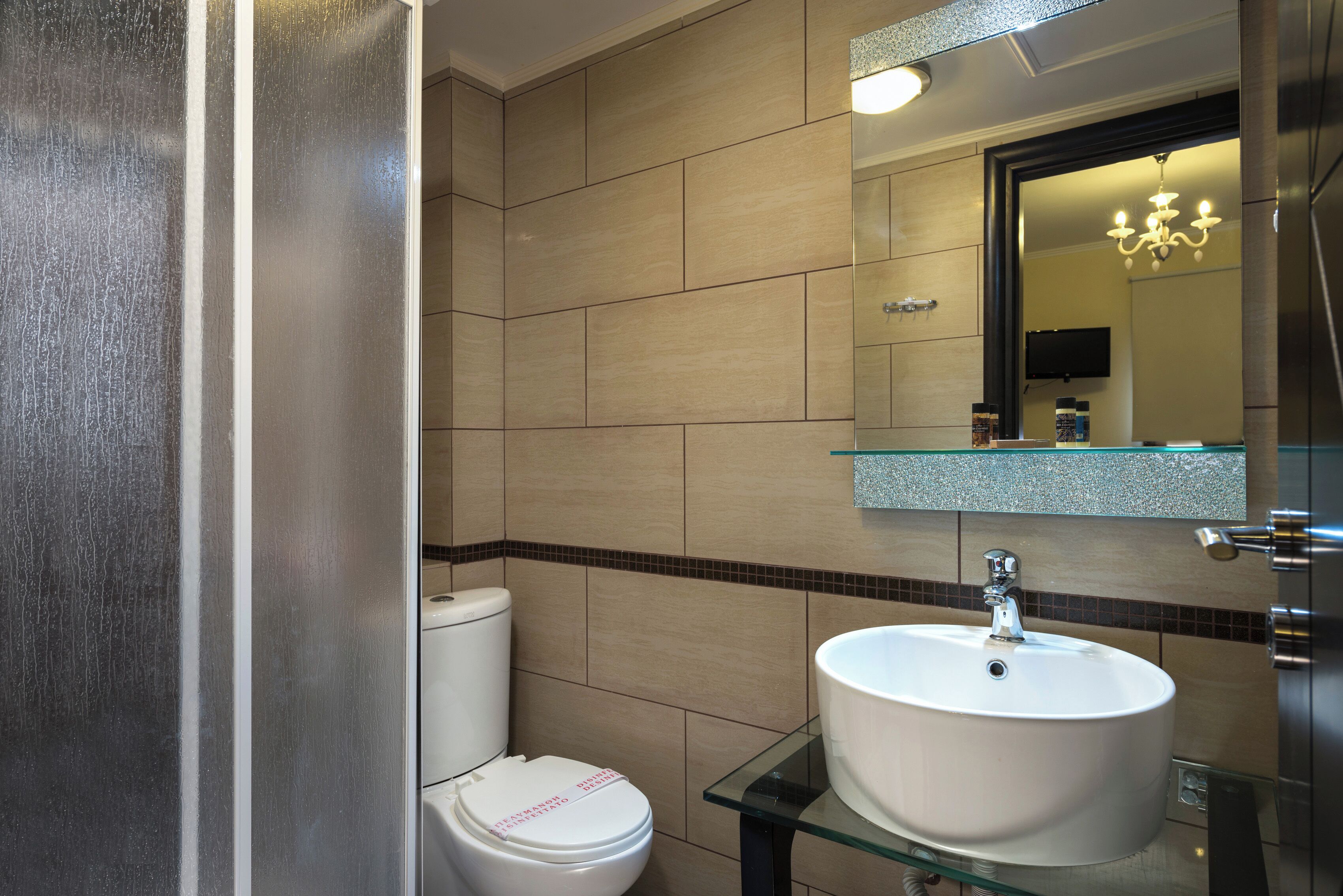 A modern bathroom with a toilet, a glass sink, and a mirror above the sink.