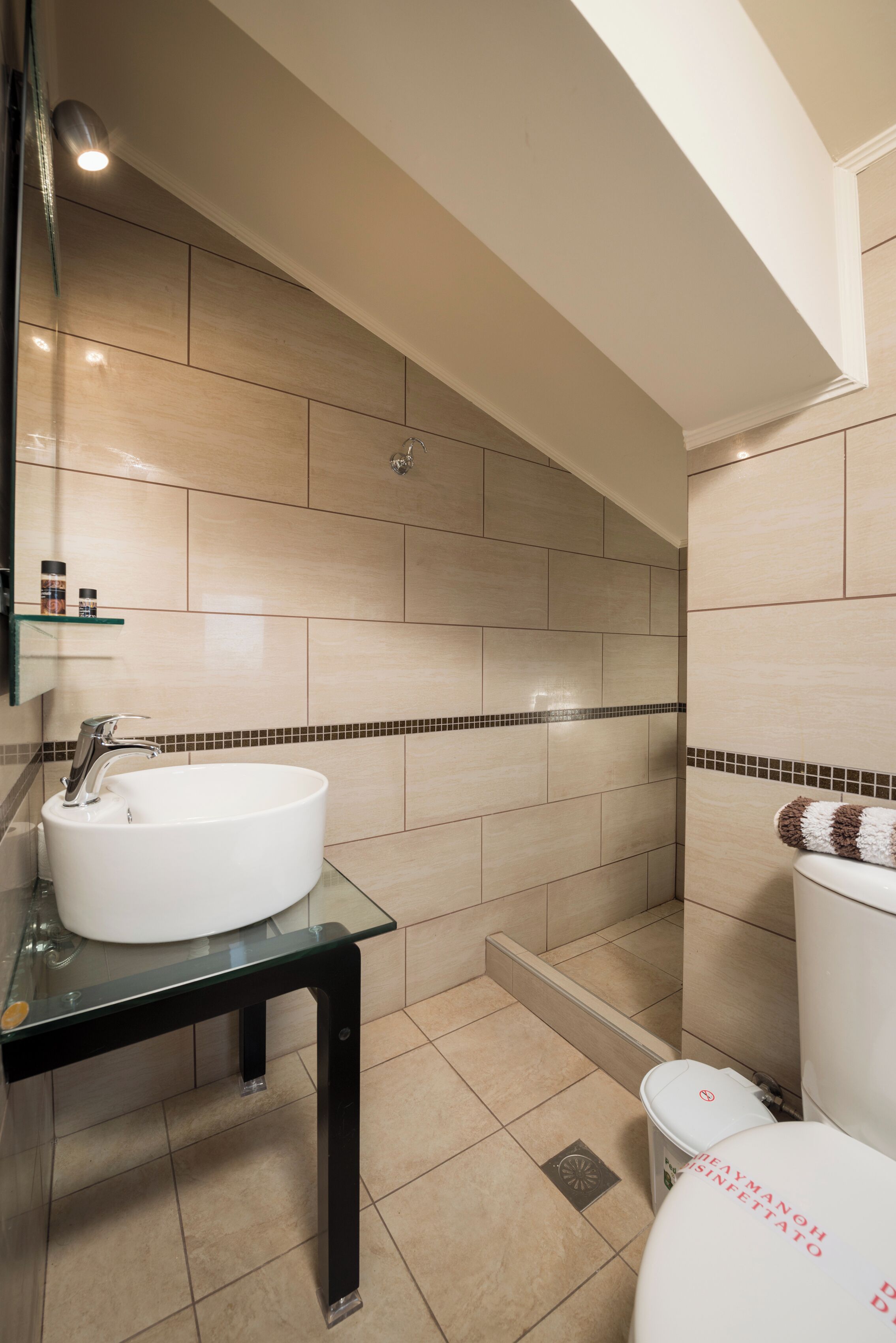 A bathroom with a white sink, a glass countertop, a toilet, and a shower area.