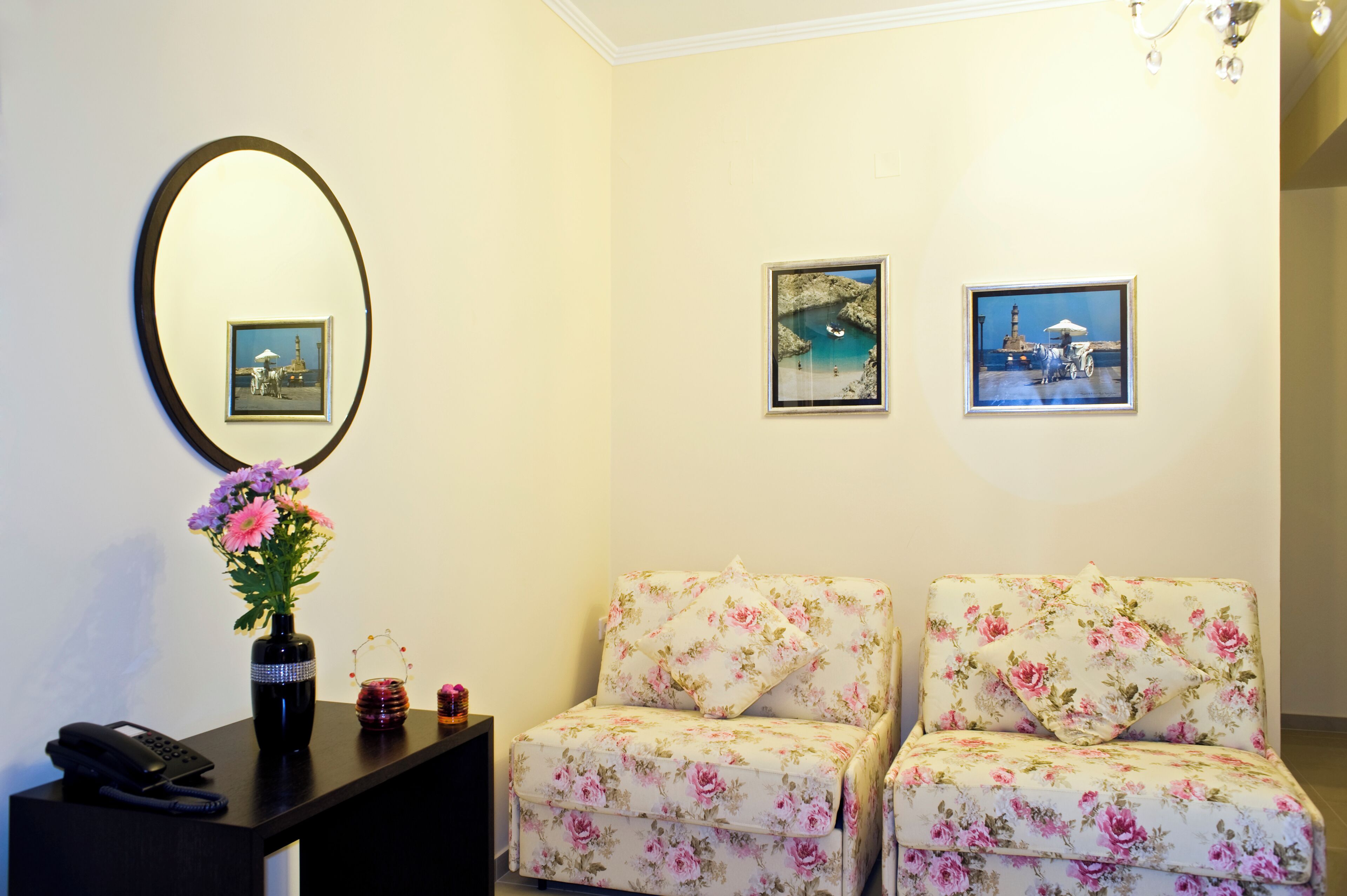 A room with two floral-patterned chairs, a vase with flowers, a framed picture, and a mirror on the wall.