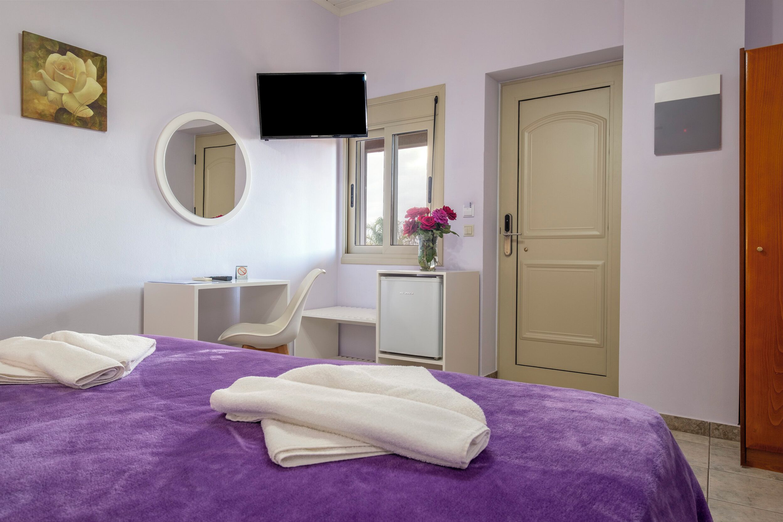 Habitación de hotel con cama, escritorio, silla, televisor, espejo y puerta.