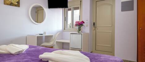 Habitación de hotel con cama, escritorio, silla, televisor, espejo y puerta.