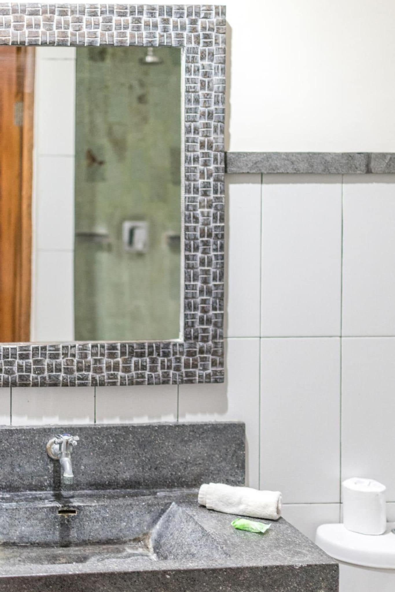 Casa de banho com parede revestida de azulejos, pia com torneira e espelho com moldura em mosaico.