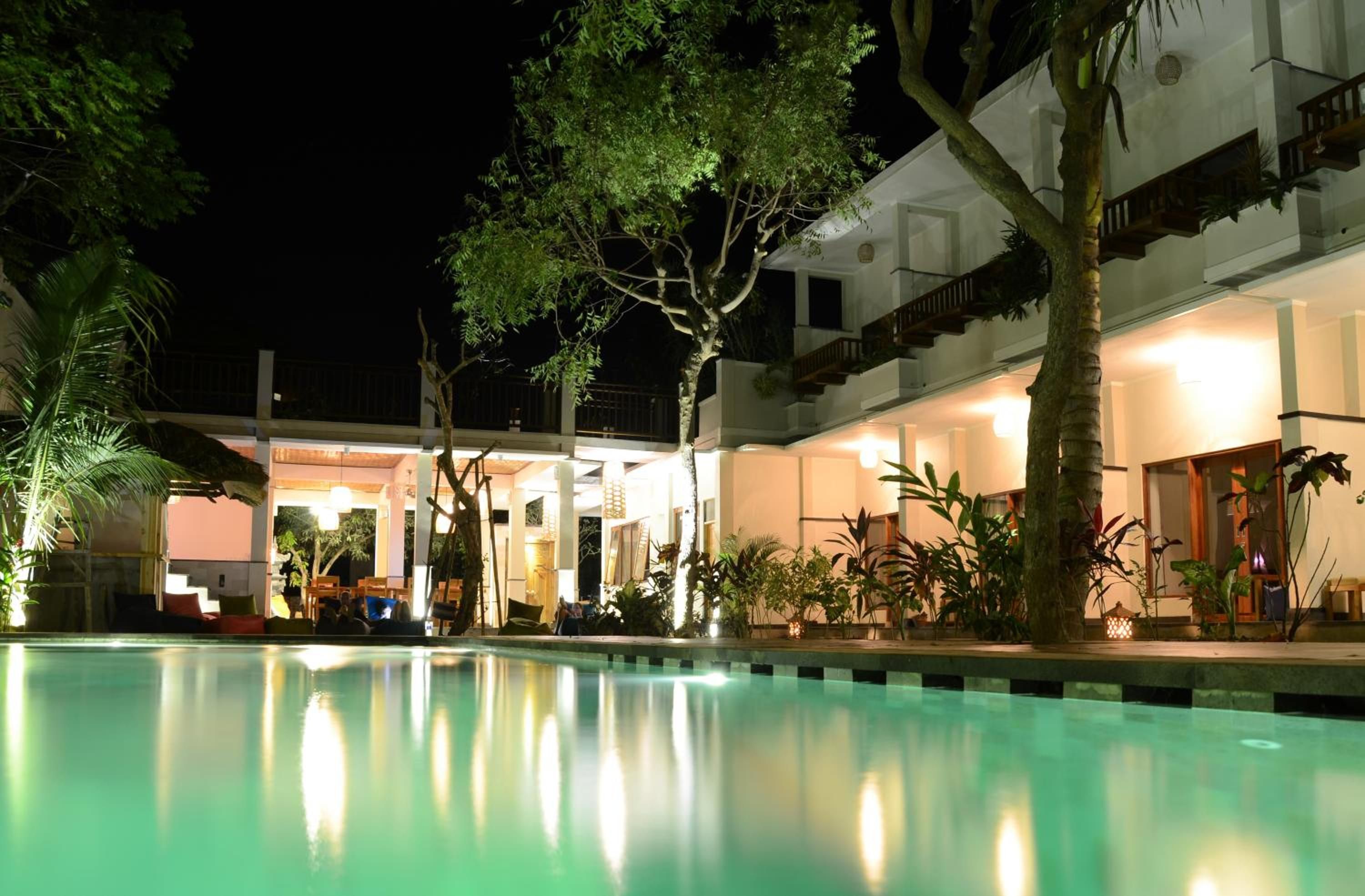 A pool area with a building in the background, surrounded by trees and plants.
