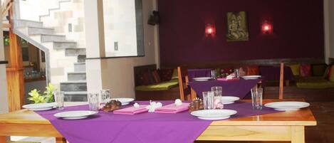 A restaurant with purple tablecloths, wooden tables, and green cushioned chairs.