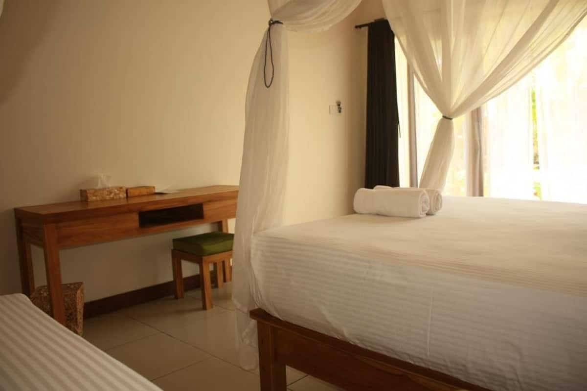 A bedroom with a bed, a wooden desk, a green chair, and a window with curtains.