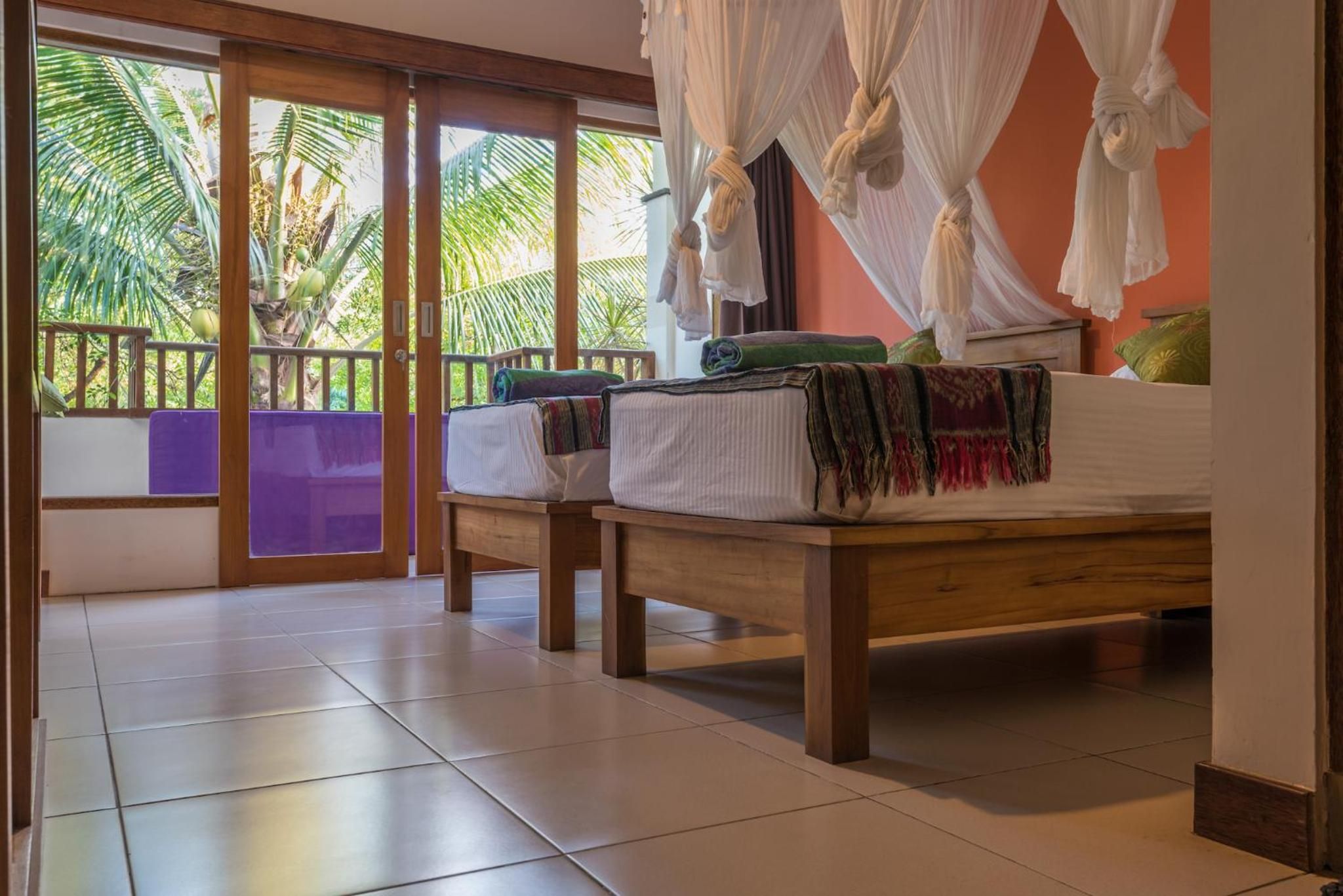 Een kamer met twee bedden, een balkon met uitzicht op palmbomen en een schuifdeur van glas.