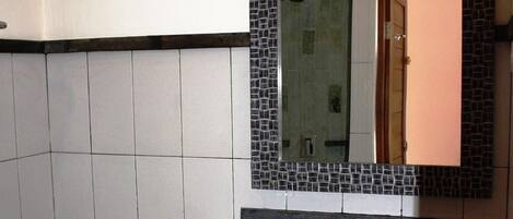 A bathroom with a tiled wall, a sink with a faucet, a toilet, and a mirror with a mosaic frame.