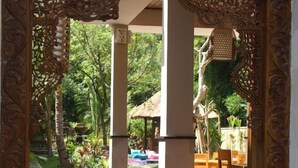An ornate wooden archway leading to a covered outdoor seating area with stone steps and a thatched roof. - Arjuna Homestay (Pemuteran)