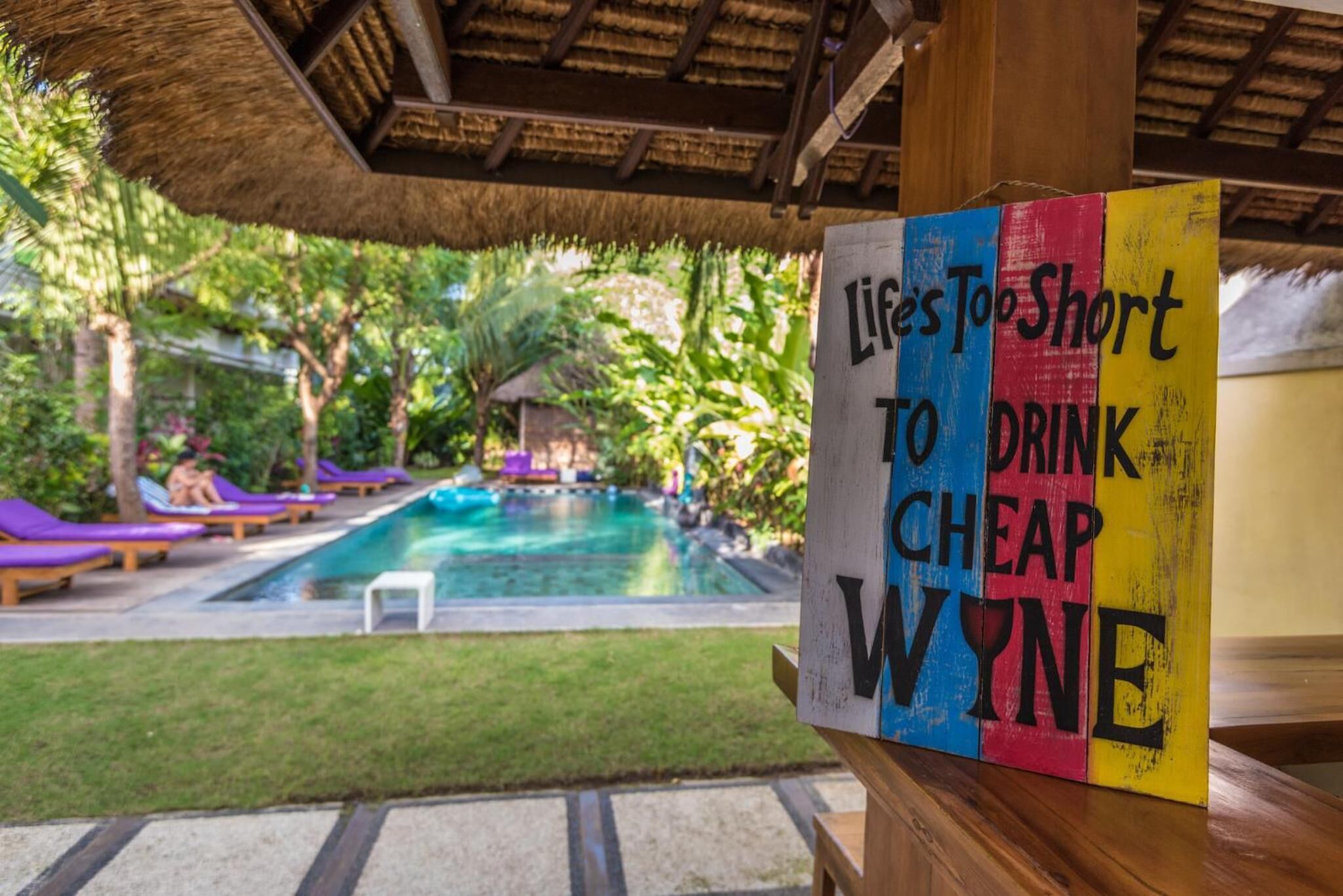 Zona de piscina con un cartel que dice "La vida es demasiado corta para beber vino barato."