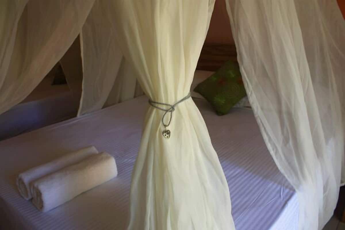 A bed with a white bedspread, a rolled towel, and a green pillow.
