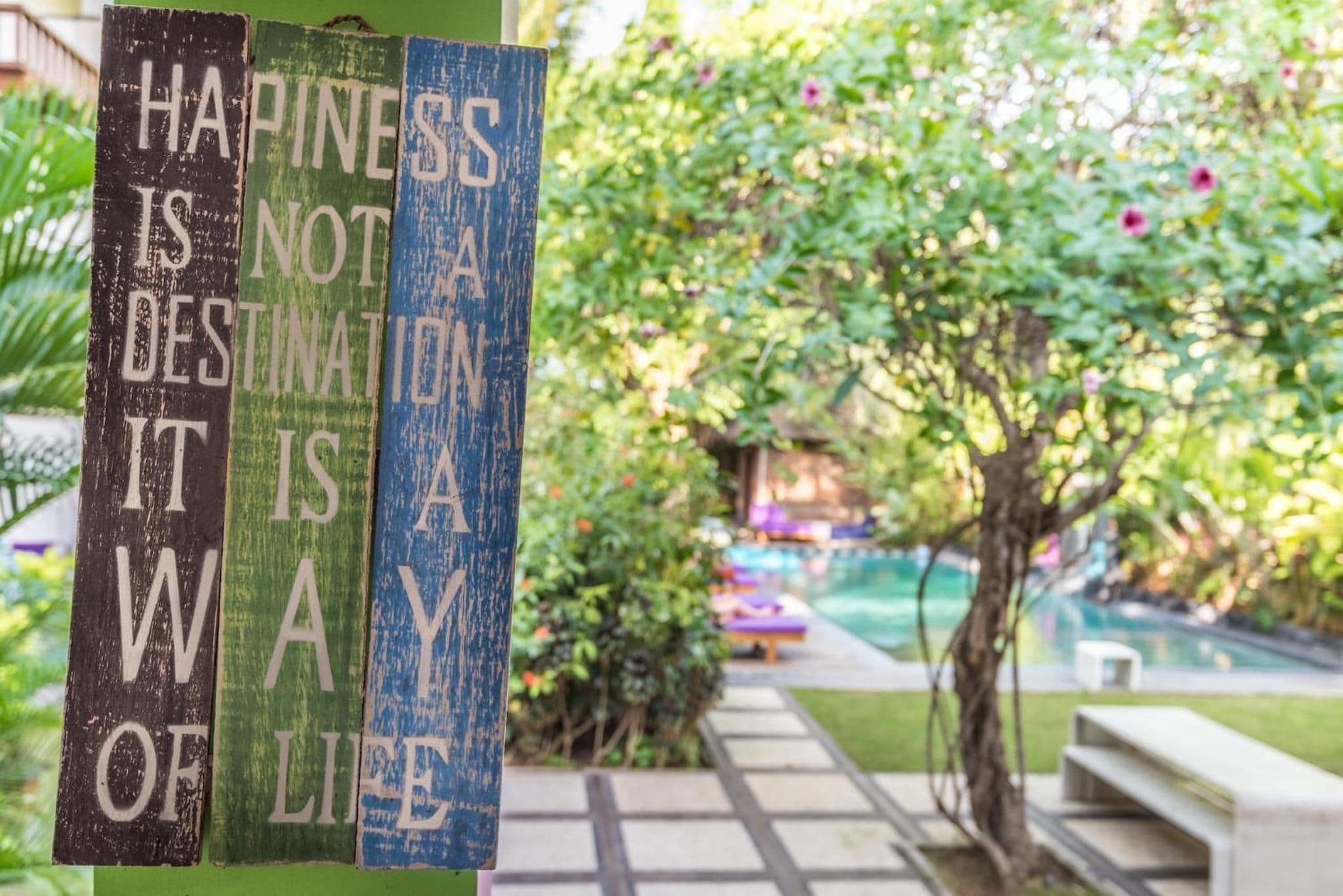 A wooden sign with a motivational quote in a garden setting with a pool and greenery.