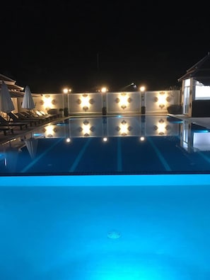 A nighttime swimming pool with star-shaped lights and lounge chairs.