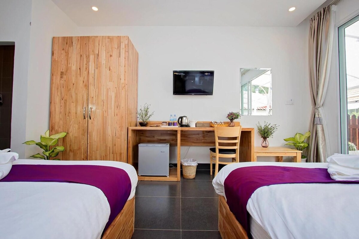 A hotel room with two beds, a desk, a television, and a window with curtains.