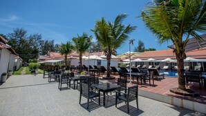 Een buitenzwembad met ligbedden en parasols, omringd door palmbomen en een betegeld pad.