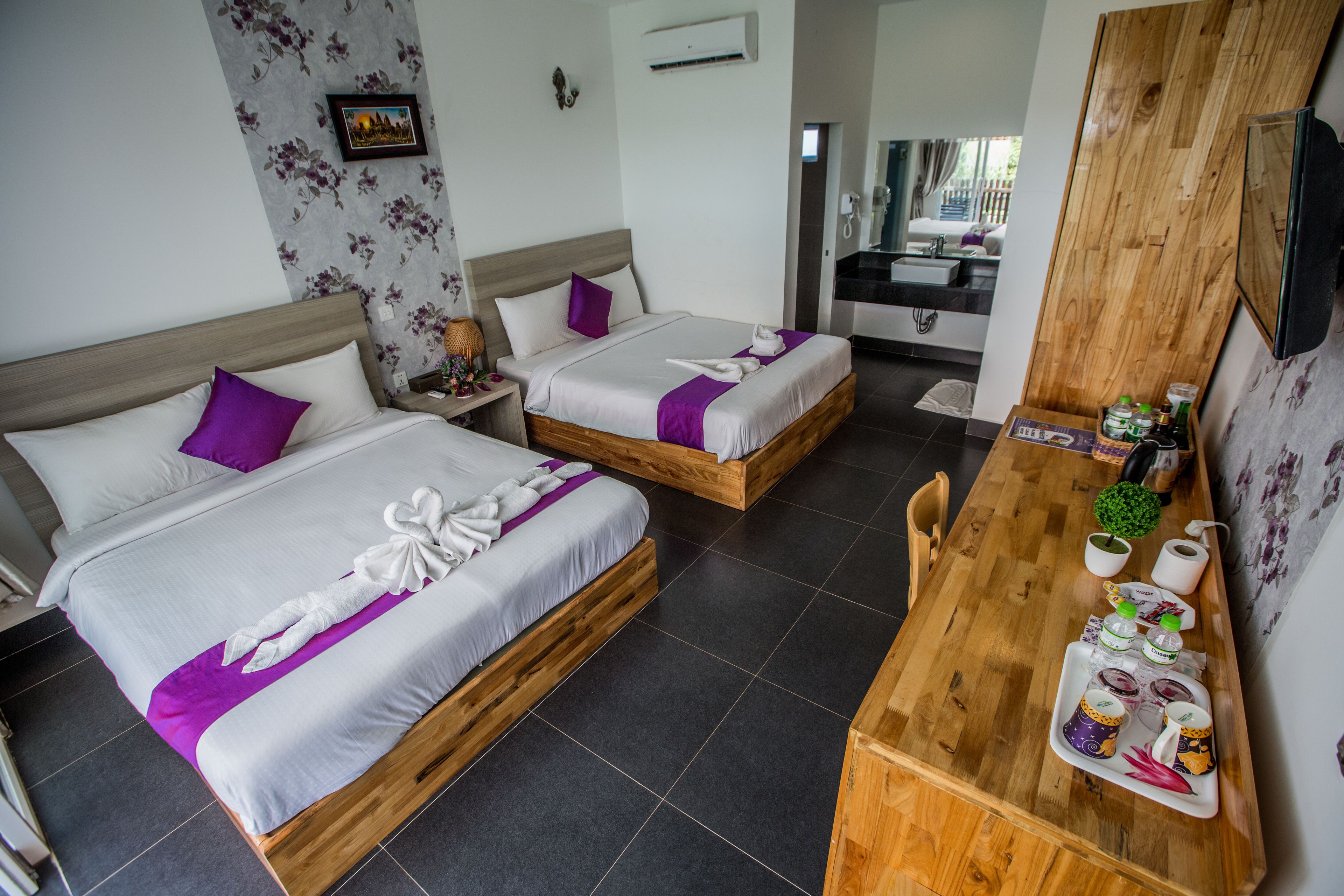A hotel room with two beds, a wooden dining table, and a bathroom visible through an open door.