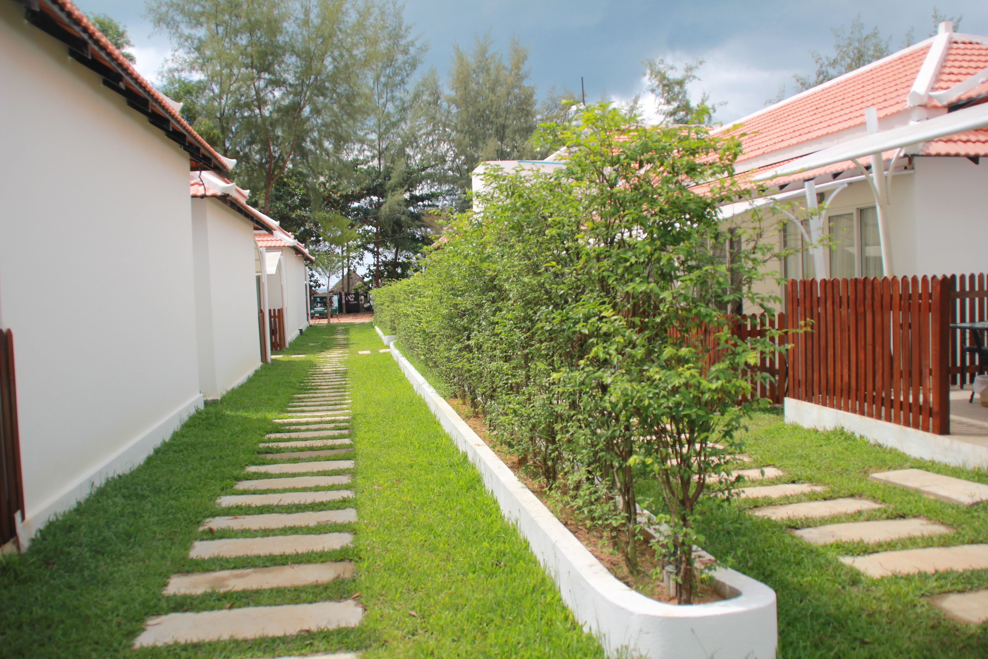 A pathway lined with neatly trimmed grass and stepping stones leading to a white building with a red-tiled roof.