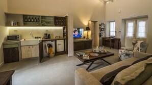 A modern kitchen with a built-in microwave, sink, and dishwasher. There is a dining area with a table and chairs, and a living room with a sofa and a television.