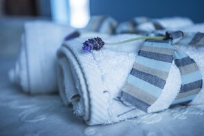 A neatly folded towel with a striped fabric and a lavender flower on a bed.