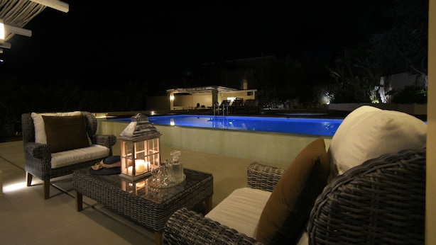 An outdoor seating area with wicker furniture, a pool, and a building in the background.