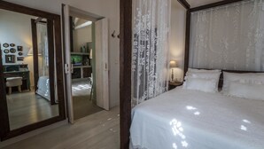 A bedroom with a large bed, a wooden headboard, and a mirror. There is a desk and chair in the adjacent room.