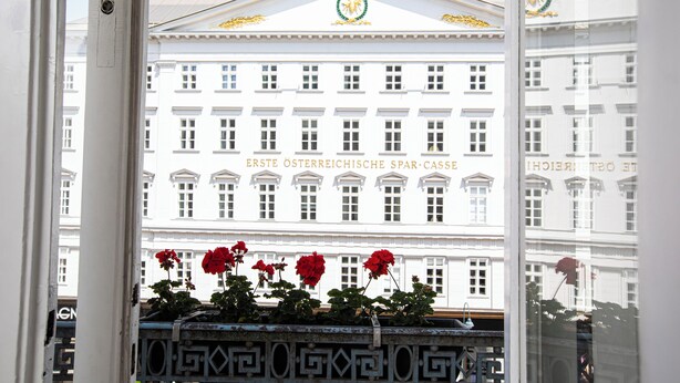 Un bâtiment à la façade classique, doté d’une entrée centrale surmontée d’un fronton décoratif et d’une enseigne indiquant « ERSTE ÖSTERREICHISCHE SPAR-CASSE ».