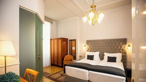 Une chambre d’hôtel avec un grand lit, une armoire en bois, une table à manger avec des chaises et un lustre.