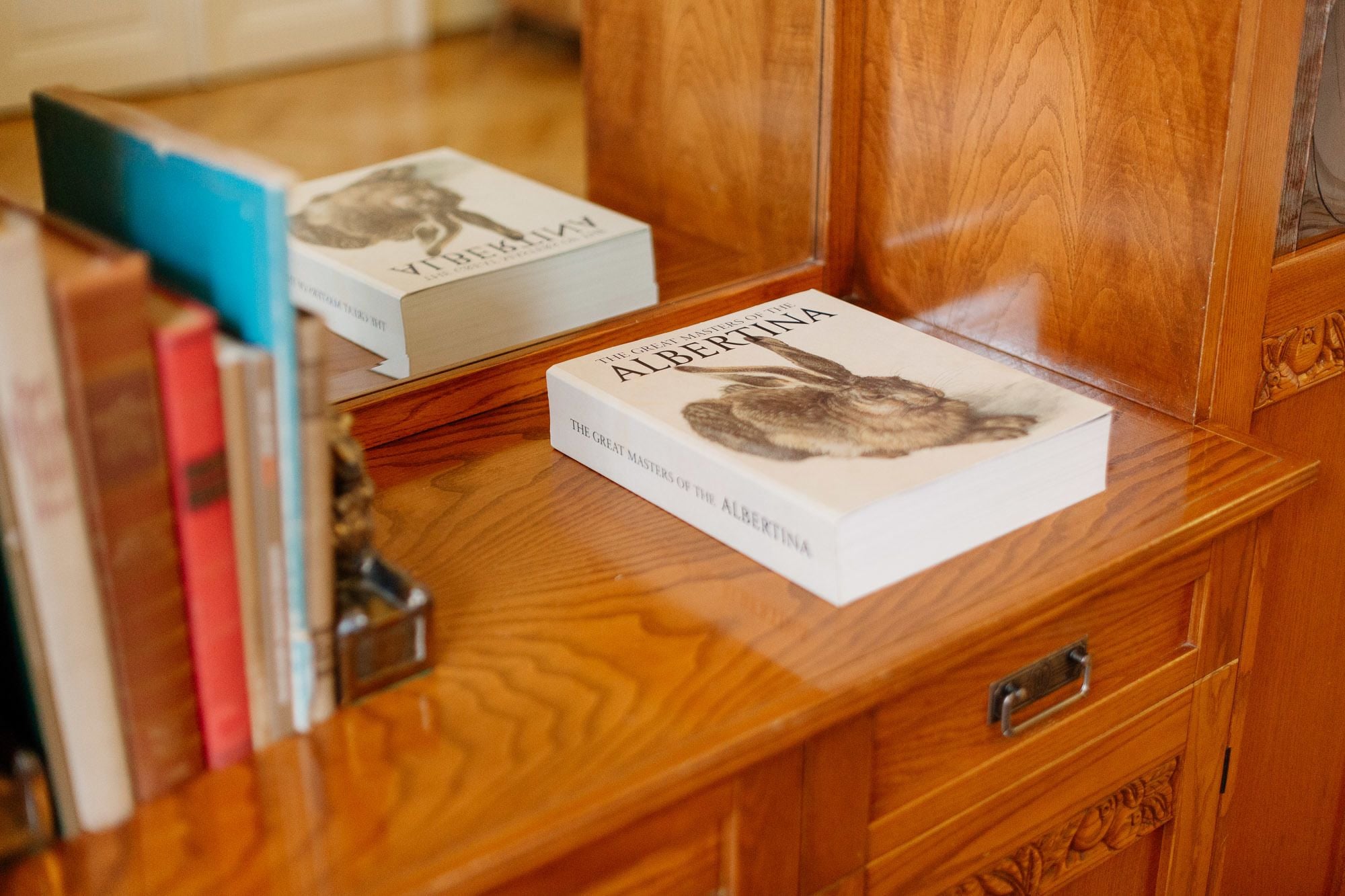 A wooden desk with a book titled 'The Great Masters of the Albertina' and a mirror reflecting the book.