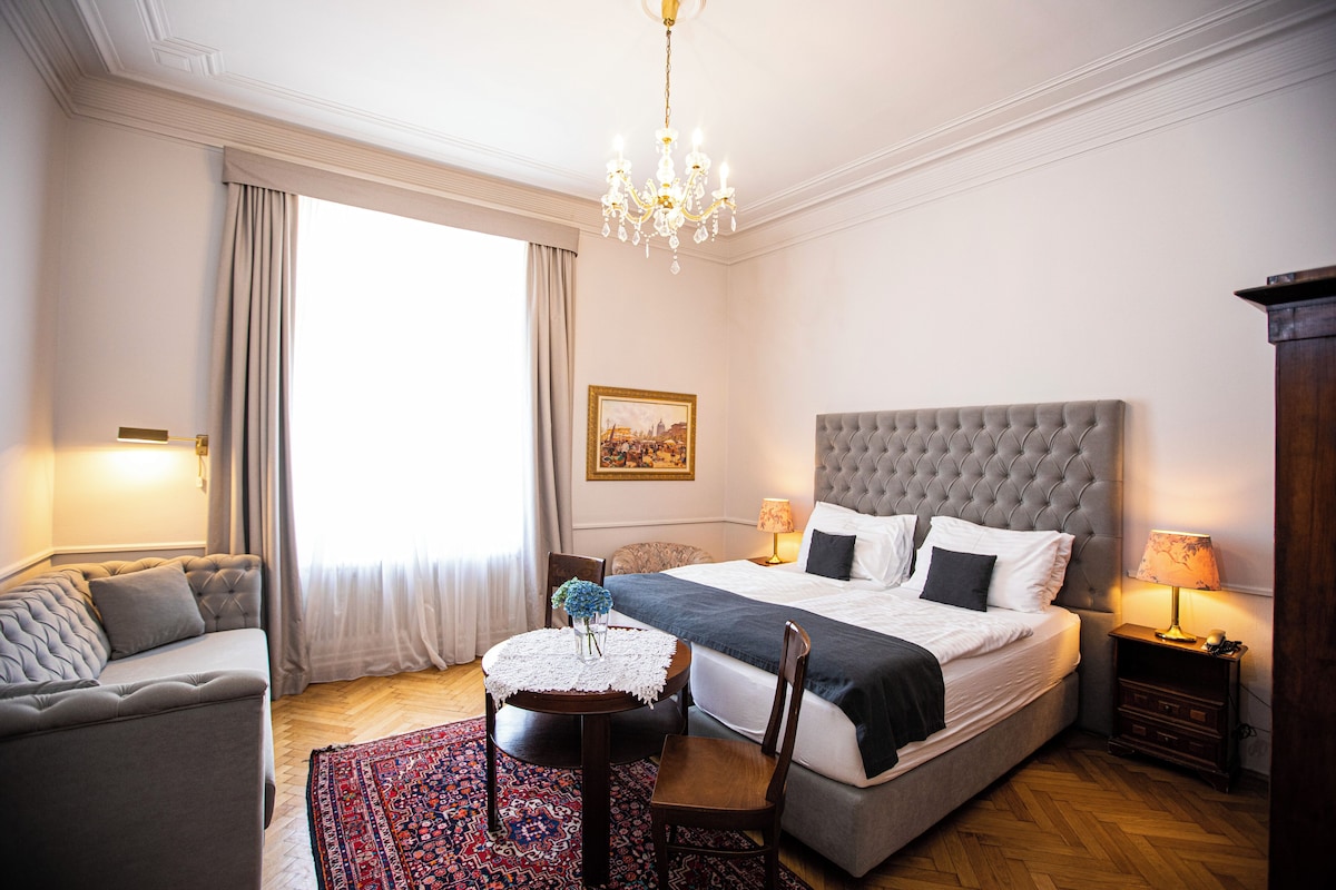 Habitació d'hotel amb un llit gran, un sofà, una taula petita amb un ram i un penjador.