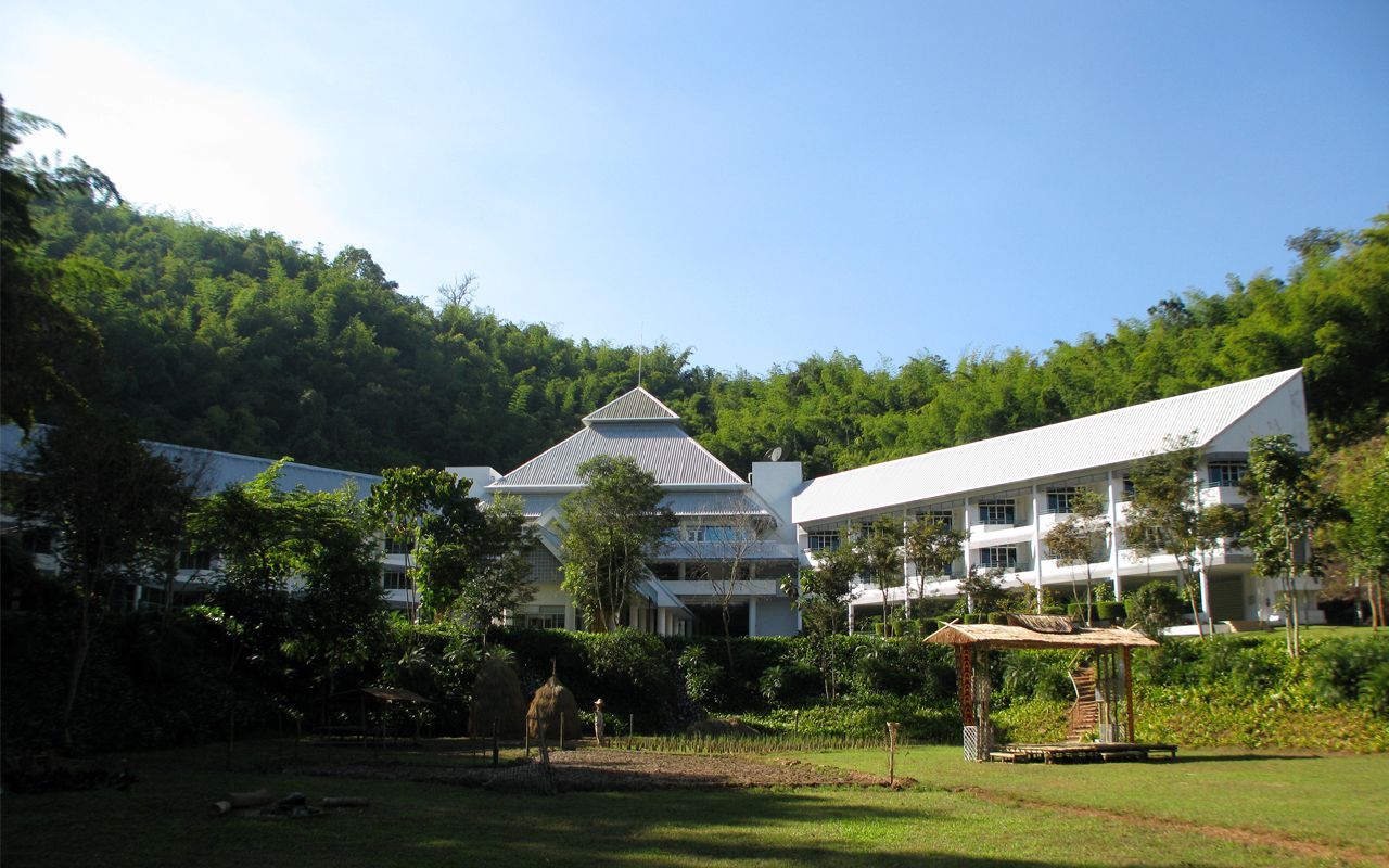 A large building with a traditional roof, surrounded by lush greenery and a clear sky.