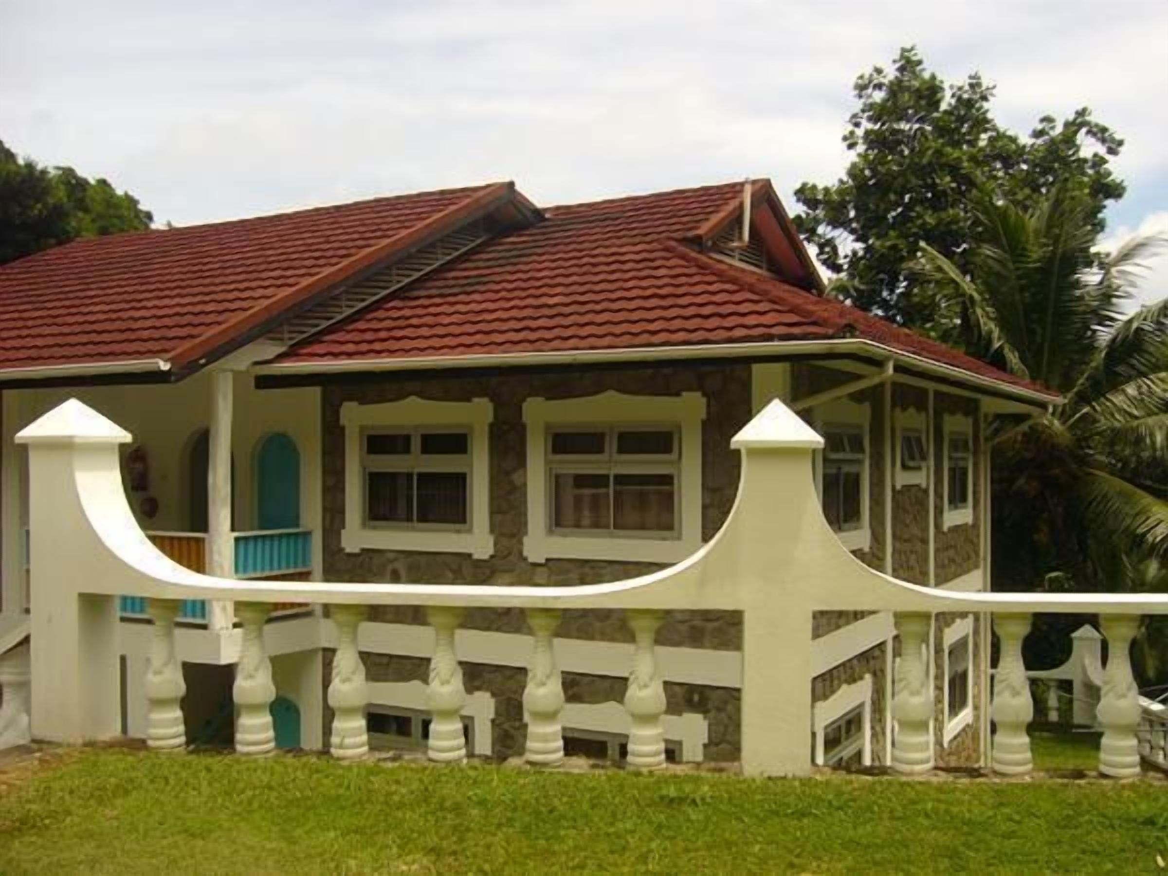 Uma casa de dois andares com telhado de telhas vermelhas, paredes externas brancas e cerca branca com balaústres.